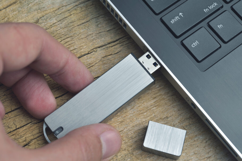 Close-up van metalen USB-flashdrive die op laptop op houten bureau wordt aangesloten.